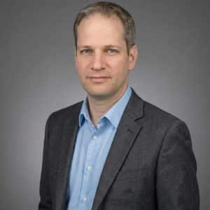 פרופ' ניר סורקין בחולצה כחולה וז'קט אפור על רקע אפור