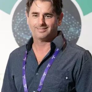 Smiling man in blue shirt wearing a purple lanyard.